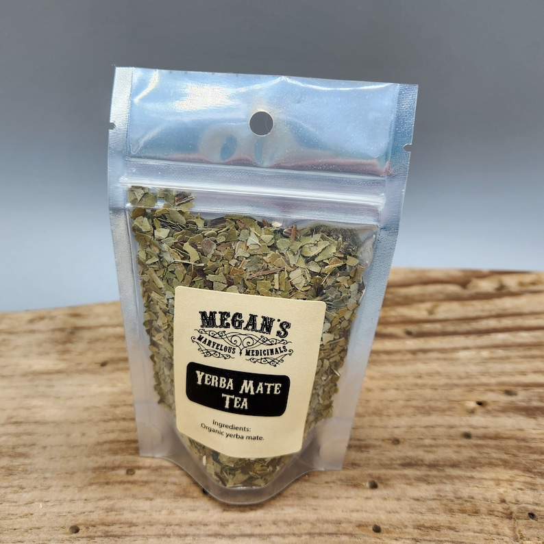 A clear plastic bag filled with loose green yerba mate tea leaves. The bag has a label that reads "Megan's Marvelous Medicinals Yerba Mate Tea" and "Ingredients: Organic yerba mate."