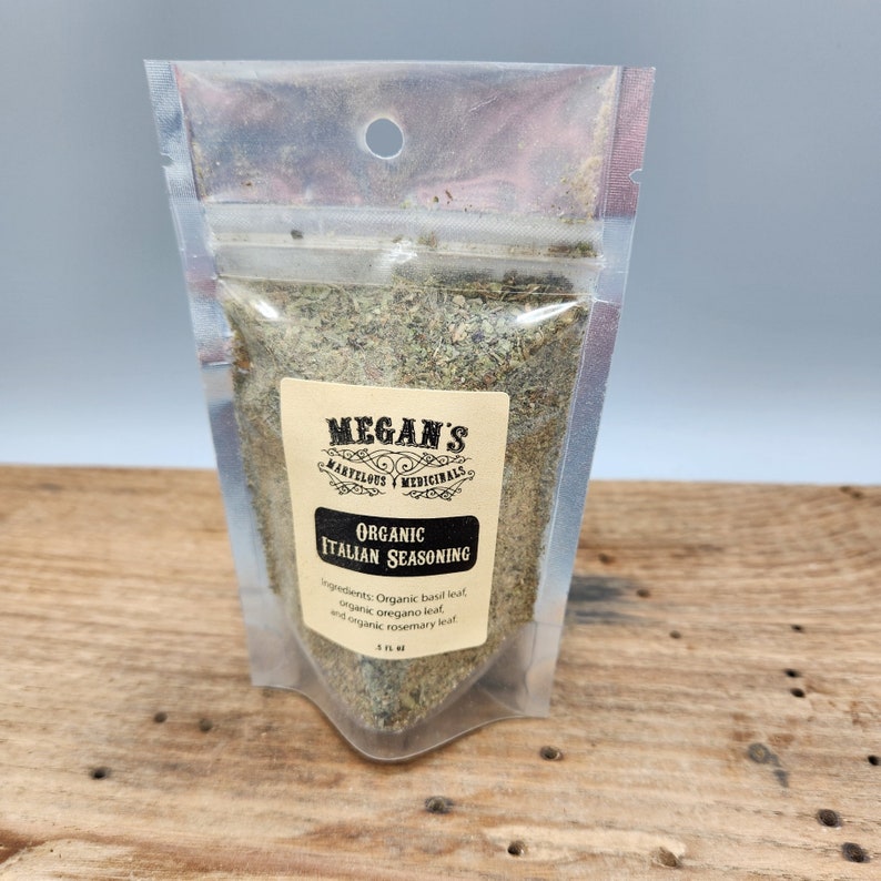 A clear plastic bag filled with dried herbs, labeled "MEGAN'S MARVELOUS MEDICINALS ORGANIC ITALIAN SEASONING". The label lists the ingredients: organic basil leaf, organic oregano leaf, and organic rosemary leaf.