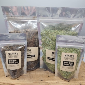 May include: Four clear plastic pouches filled with different types of tea leaves. The pouches are labeled with text that reads "Megan's Yaupon Tea". The tea leaves vary in color from dark brown to light green, and the pouches are sealed.