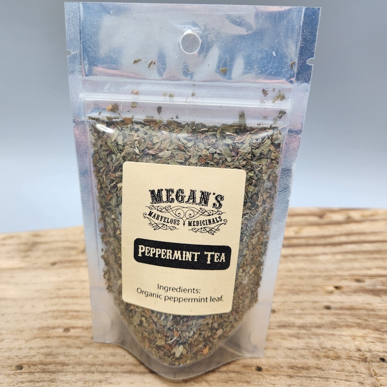 A clear plastic bag filled with dried green peppermint leaves. The bag has a label that reads "Megan's Marvelous Medicinals Peppermint Tea" and "Ingredients: Organic peppermint leaf."