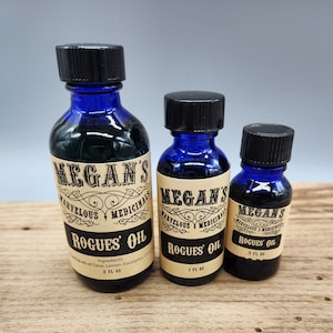 May include: Three blue glass bottles with black lids and brown paper labels. The labels have the text "Megan's Marvelous Medicinals" and "Rogues' Oil". The bottles are labeled with different sizes: 2 fl oz, 1 fl oz, and 5 fl oz.