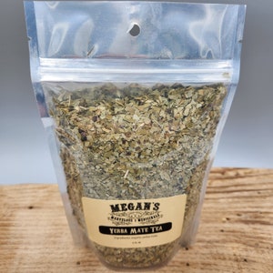 A clear plastic bag filled with loose green yerba mate tea leaves. The bag has a label that reads "Megan's Marvelous Medicinals Yerba Mate Tea" with the ingredients listed as "organic yerba mate".