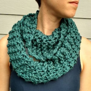 May include: A teal blue knitted infinity scarf. The scarf is made of a soft, chunky yarn and is perfect for keeping warm in the winter.