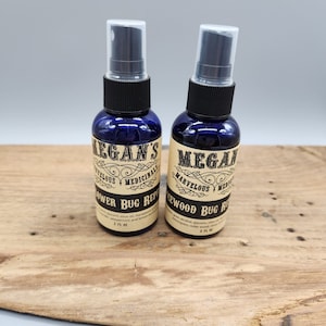 May include: Two 2 fl oz blue glass bottles with black spray tops. The bottles are labeled with a brown paper label that says "Megan's Marvelous Medicinals" and "Flower Bug Repellent" or "Cedarwood Bug Repellent".