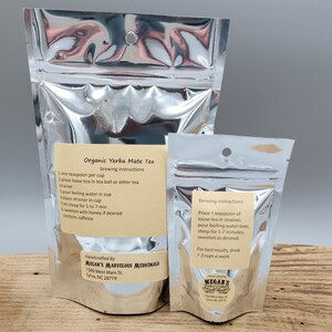 Two silver foil pouches with labels for organic yerba mate tea. The larger pouch has brewing instructions and information about the product. The smaller pouch has brewing instructions and the company logo. Both pouches have the company name "Megan's Marvelous Medicinals" and address.