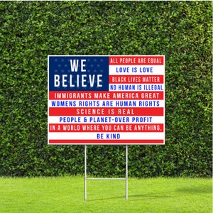 May include: A red, white and blue yard sign with the text "WE BELIEVE" in large white letters. The sign also includes a list of statements about equality, love, and human rights, including "All people are equal", "Love is love", "Black lives matter", "No human is illegal", "Immigrants make America great", "Women's rights are human rights", "Science is real", "People & planet-over profit", "In a world where you can be anything", and "Be kind".