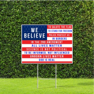 May include: A red, white, and blue yard sign with the text "We Believe" and a list of statements including "To Salute the Flag", "To Stand for Freedom", "Police Protect Us", "In Borders", "In the 2nd Amendment", "All Lives Matter", "Science is not Political", "To be Informed, Not Influenced", "Unborn Lives Matter", and "God is Real".