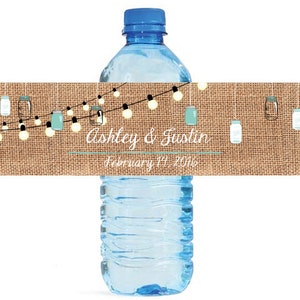 May include: A burlap wedding water bottle label with string lights and mason jars. The label reads "Ashley & Justin, February 17, 2016".