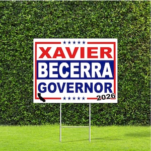 Może przedstawiać: Biały szyld ogrodowy z czerwonym i niebieskim napisem "XAVIER BECERRA GOVERNOR 2026". Szyld ma czerwoną obwódkę i grafikę stanu Kalifornia. Jest zamontowany na metalowym słupku i umieszczony na zielonym trawniku.