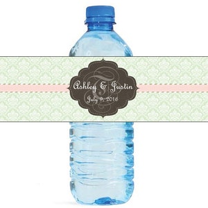 Könnte beinhalten: Ein Wasserflaschenetikett mit grünem und weißem Damastmuster, einem rosa Band und einem braunen, monogrammierten Etikett mit der Aufschrift "Ashley & Justin July 9, 2016".