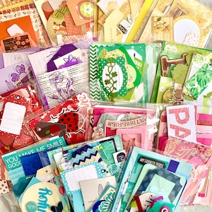 May include: A collection of colorful paper ephemera, including tags, die cuts, and patterned papers. The assortment features various shapes, sizes, and designs, with text like "YOU MAKE ME SMILE" and "MY FAVORITE PEOPLE". The color palette includes pinks, greens, blues, and oranges.