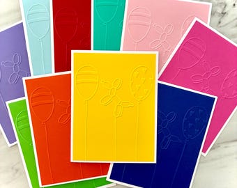 May include: A collection of colorful greeting cards with embossed balloon designs. The cards are in various colors, including yellow, pink, blue, green, and red, with white borders. Some cards feature a balloon animal design.
