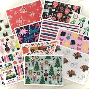 May include: A collection of decorative greeting cards with various patterns. Designs include snowflakes, palm trees, Valentine's Day hearts, bunnies, school supplies, a truck with pumpkins, turkeys, and Christmas themes.