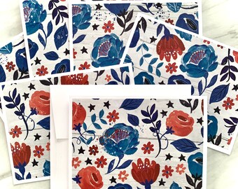 May include: A collection of floral greeting cards and envelopes. The cards feature a watercolor design with blue and red flowers, black stars, and leaves on a white wood-grain background. The envelopes are white.