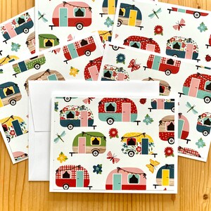 May include: A collection of greeting cards and envelopes featuring a colorful camper design. The campers are decorated with floral patterns, polka dots, and gingham, with accents of butterflies, dragonflies, and flowers. The cards are on a white background.
