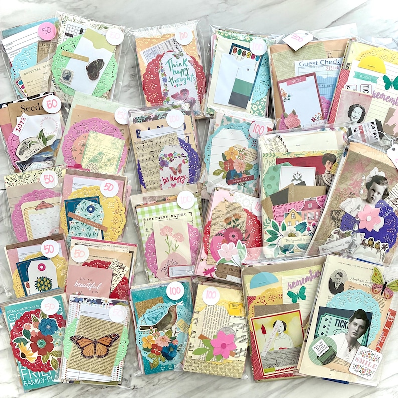 May include: A collection of assorted paper ephemera packs, each sealed in a clear bag. The packs contain decorative tags, cards, and paper elements with floral, butterfly, and vintage-inspired designs. Some packs have price tags.