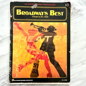 May include: A music book titled Broadway's Best, arranged by Bill Irwin, from the Hal Leonard Organ Adventure Series. The cover features a black silhouette of a person playing a trumpet against an orange background with text overlays.