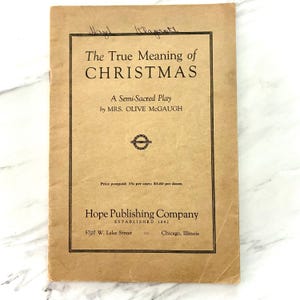 May include: A tan paper-covered booklet titled The True Meaning of CHRISTMAS, A Semi-Sacred Play by MRS. OLIVE McGAUGH. The cover features black text, a small circular emblem, and the Hope Publishing Company name with Chicago, Illinois address.