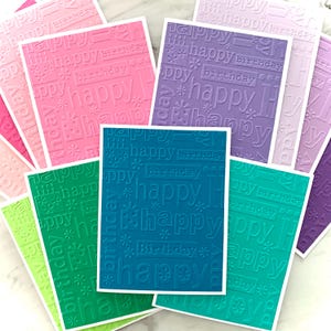 May include: A collection of colorful birthday cards in shades of pink, purple, green, and teal. Each card features the words "happy birthday" embossed in a repeating pattern. The cards have white borders.