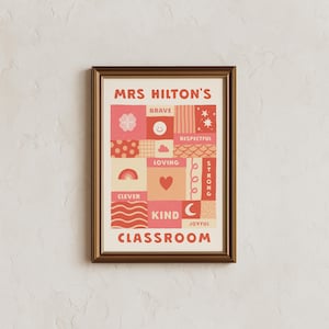 May include: A framed wall art print featuring the text MRS HILTON'S CLASSROOM in red. The design consists of a grid of squares and rectangles in shades of pink, red, and cream, decorated with icons like a rainbow, heart, stars, and smiley face.
