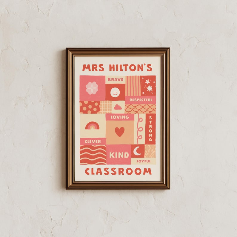 May include: A framed wall art print featuring the text MRS HILTON'S CLASSROOM in red. The design consists of a grid of squares and rectangles in shades of pink, red, and cream, decorated with icons like a rainbow, heart, stars, and smiley face.