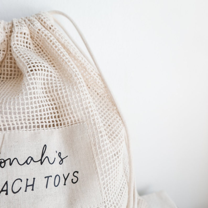 May include: A white mesh drawstring bag with a white fabric pocket that says "Jonah's Beach Toys" in black text.