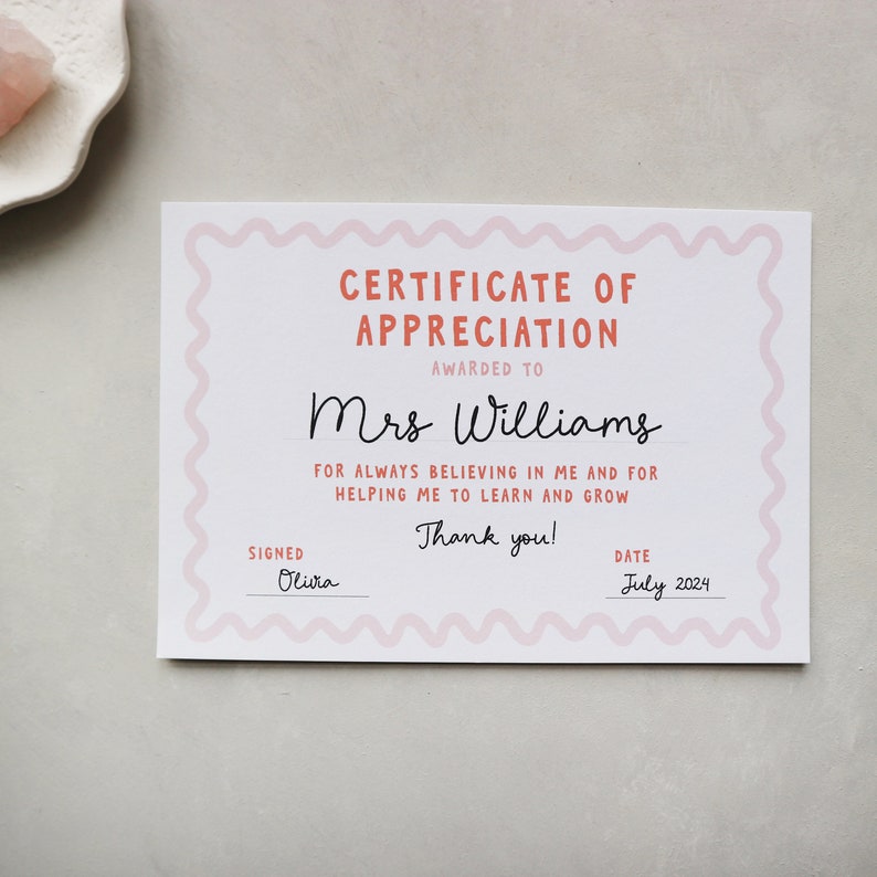 May include: A pink and white certificate of appreciation with a wavy border. The certificate is awarded to Mrs. Williams for always believing in the recipient and helping them learn and grow. The certificate is signed by Olivia and dated July 2024.