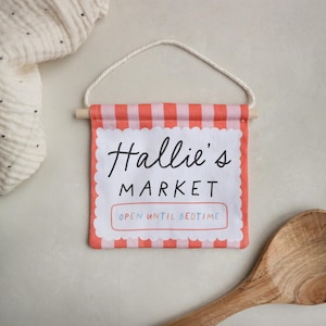 May include: A pink and white striped fabric banner with the text "Hallie's Market" and "Open Until Bedtime".