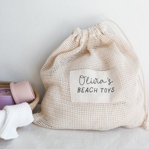 May include: A beige mesh drawstring bag with a white label that says "Olivia's Beach Toys".