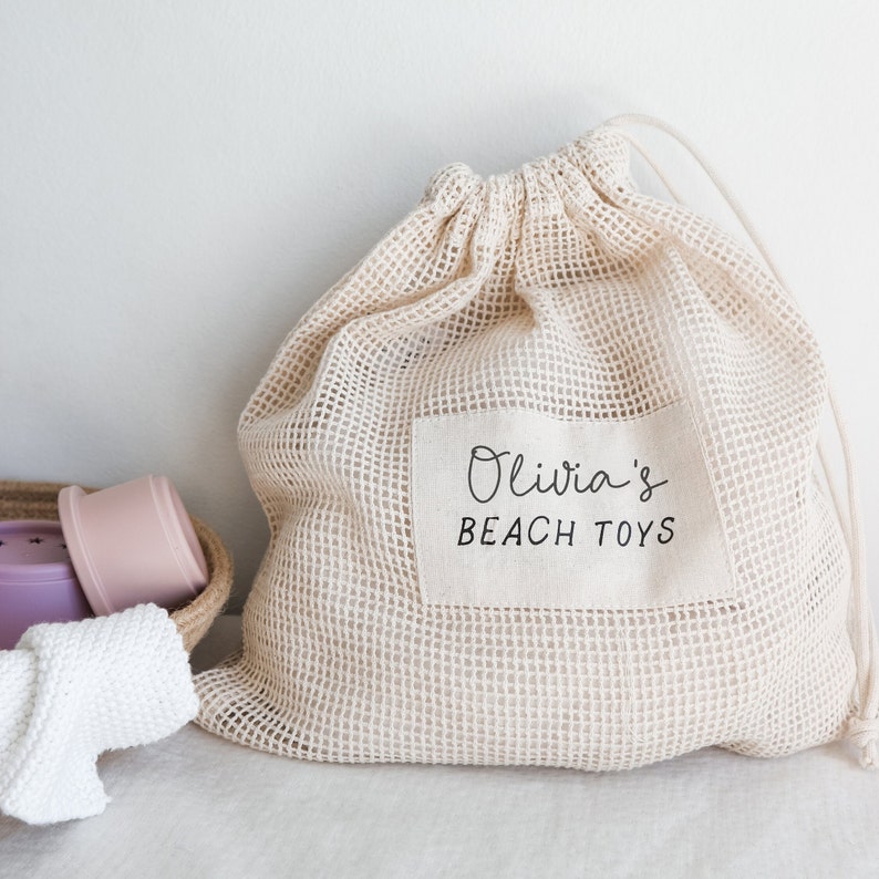 May include: A beige mesh drawstring bag with a white label that says "Olivia's Beach Toys".