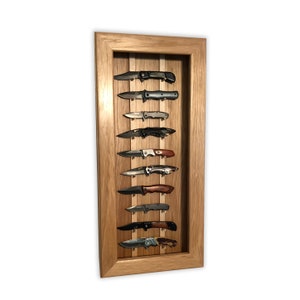 May include: A wooden display case with a light oak finish, showcasing ten pocket knives. The knives are arranged vertically, each secured in place. The blades and handles vary in design, with black, silver, and wood tones.