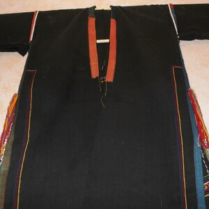 May include: A black long-sleeved garment with colorful trim and tassels. The garment has a V-neck and is made of a woven fabric.