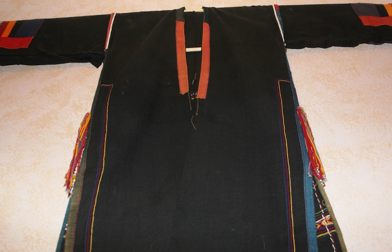 May include: A black long-sleeved garment with colorful trim and tassels. The garment has a V-neck and is made of a woven fabric.