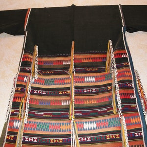 May include: A black robe with colorful geometric patterns and white beaded fringe. The robe has a long, flowing design and is made of a soft, woven fabric.