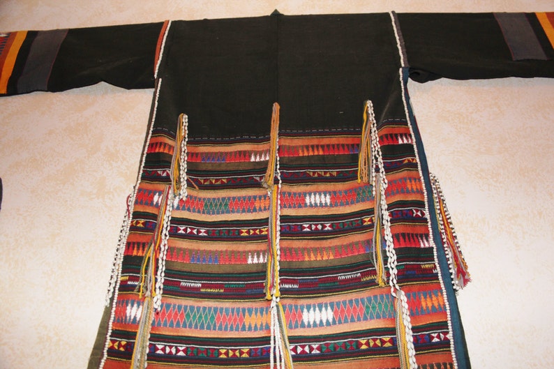 May include: A black robe with colorful geometric patterns and white beaded fringe. The robe has a long, flowing design and is made of a soft, woven fabric.