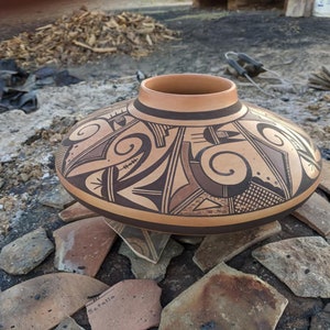 Op de afbeelding: Een grote, ronde, bruine aardewerken kom met een geometrisch ontwerp in zwart en wit. De kom staat op een stapel gebroken aardewerk scherven.