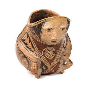 May include: A hand-painted ceramic pot with a human face and geometric patterns in black, brown, and white. The pot is shaped like a person sitting with their legs crossed.