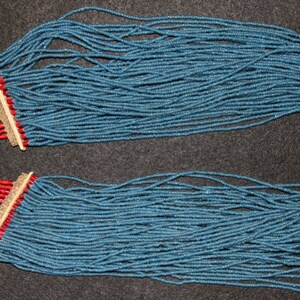 May include: A long necklace made of blue, red, green, and white beads. The necklace is made of many strands of beads and has a bone pendant at the end.