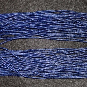 Puede incluir: Una larga hebra de cuentas de lapislázuli azul oscuro. Las cuentas son pequeñas y redondas, y están enhebradas en un hilo fino. La hebra mide aproximadamente 3 metros de largo.