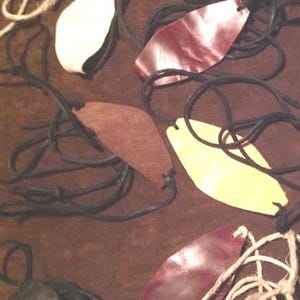Könnte beinhalten: Eine Sammlung von sechs Lederschleudern in verschiedenen Farben und Stilen. Die Schleudern sind aus braunem, rotem und gelbem Leder gefertigt und haben schwarze Gummibänder. Die Schleudern sind auf einer braunen Oberfläche angeordnet.