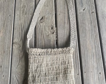 May include: A beige woven shoulder bag with a rectangular body and a long strap. The bag has a grid-like pattern and is made of a natural fiber material. The strap is also woven and attached to the top corners of the bag.