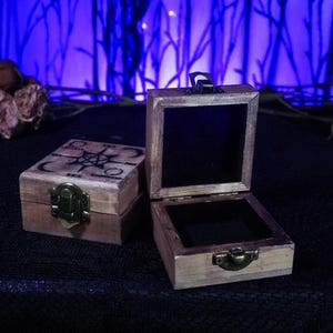 以下が含まれることがあります： 蝶番付きの蓋が付いた木製の箱が2つ。左側の箱は、上に五芒星模様が描かれている。右側の箱は開いており、黒いベルベットの内側が見える。