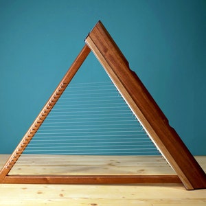 May include: A triangular wooden harp with strings stretched across the frame. The harp is made of dark wood and has a natural finish.