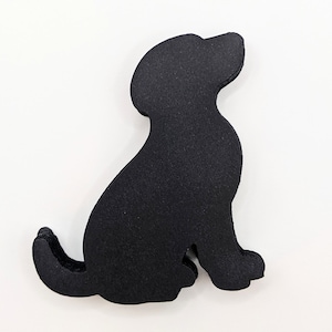 May include: Black paper cutout of a dog sitting with its head turned to the side. The dog is facing the right side of the image.