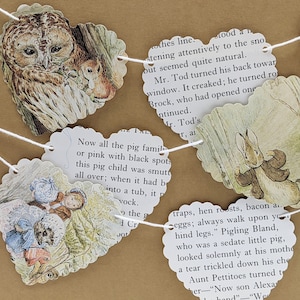 May include: A heart-shaped garland featuring illustrations of woodland creatures and scenes from a storybook. The garland is strung with white twine and includes images of an owl, a rabbit, and children.