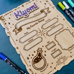 Puede incluir: Letrero de madera 'Mis cosas favoritas' con detalles grabados. Cuenta con espacios para 'Libro', 'Amigo', 'Actividad' y 'Animal'. Incluye una sección para 'Color favorito' y una placa con el nombre 'Kiyomi'. Se ven marcadores.