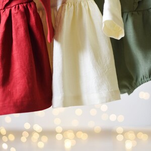 May include: Three linen dresses hanging on a clothesline. The dresses are red, white, and green. The background is blurred and has a bokeh effect.