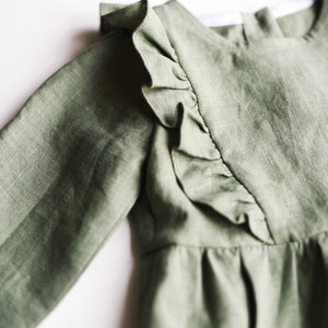 May include: A sage green linen dress with a ruffled neckline and long sleeves.