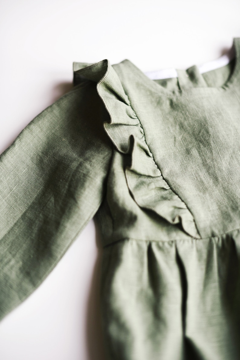 May include: A sage green linen dress with a ruffled neckline and long sleeves.