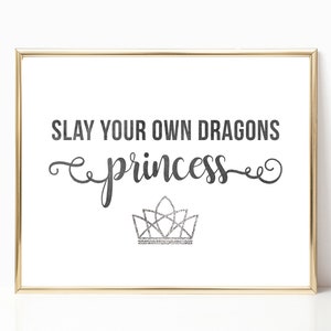 May include: A framed print with the text "SLAY YOUR OWN DRAGONS princess" in black script with a silver glitter crown underneath.